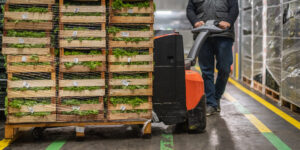 Worker Transporting Crates Of Lettuce In Warehouse